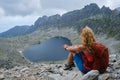 Turistka s kučeravými blond vlasmi a červeným ruksakom sa pozerá na Vyšné Wahlenbergovo jazero vo Vysokých Tatrách.