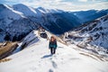 Woman hiker going up on a snowy mountain ridge, in Fagaras mountains, Romania, with the high alpine road Transfagarasan in the bac