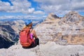 Woman hiker with helmet and red backpack looks towards Tofana di Mezzo and di Dentro in Dolomites mountains, Italy.