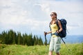 Woman hiker hiking on grassy hill, wearing backpack, using trekking sticks in the mountains Royalty Free Stock Photo