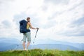 Woman hiker hiking on grassy hill, wearing backpack, using trekking sticks in the mountains Royalty Free Stock Photo