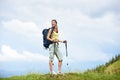 Woman hiker hiking on grassy hill, wearing backpack, using trekking sticks in the mountains Royalty Free Stock Photo