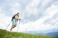 Woman hiker hiking on grassy hill, wearing backpack, using trekking sticks in the mountains Royalty Free Stock Photo