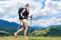 Woman hiker hiking on grassy hill, wearing backpack, using trekking sticks in the mountains Royalty Free Stock Photo