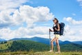Woman hiker hiking on grassy hill, wearing backpack, using trekking sticks in the mountains Royalty Free Stock Photo