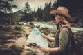 Woman hiker, searching right direction on map near wild mountain river.