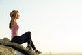 Woman hiker sitting on a steep big rock enjoying warm summer day. Young female climber resting during sports activity in nature.