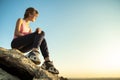 Woman hiker sitting on a steep big rock enjoying warm summer day. Young female climber resting during sports activity in nature.