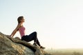 Woman hiker sitting on a steep big rock enjoying warm summer day. Young female climber resting during sports activity in nature.