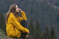 Woman hikers enjoys break look into the distance. Young pretty girl wears yellow raincoat on forest background