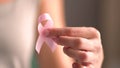 Woman hold pink ribbon. Close up view of hand with symbol of national breast canser awareness month in october