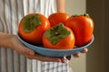 Woman hold plate with ripe persimmon, close up