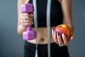 woman in holding apple and measuring tape and dumbbell standing  over gray background Royalty Free Stock Photo