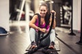 Woman holding battle ropes sits on a mat nside the gym, smiling at the camera