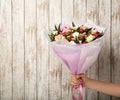 Woman holding beautiful bouquet of flowers and chocolate candies on white wooden background, closeup. Space for text Royalty Free Stock Photo