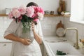 Woman holding beautiful peonies in vase at sink with brass faucet and granite countertop. Stylish female holding pink peony Royalty Free Stock Photo