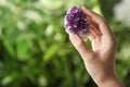 Woman holding beautiful purple amethyst gemstone on blurred green background. Space for text