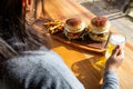 woman holding a beer, burgers and fries next to it