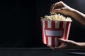 Woman holding a big bucket of salty hot popcorn against dark background.Empty space for text Royalty Free Stock Photo