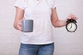 Woman holding a big gray cup of coffee and alarm clock showing 7 am in hands, ready for work with caffeine energy concept Royalty Free Stock Photo