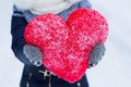 Woman is holding big heartshape pillow outdoors in winter.