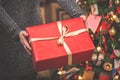 Woman holding a big red gift box against amazing christmas tree background. Toned and selective focus Royalty Free Stock Photo