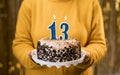 Woman holding birthday cake with burning candles number 13 against decorated background, close up. Celebrates birthday Royalty Free Stock Photo