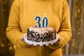 Woman holding birthday cake with burning candles number 30 against decorated background, close up. Celebrates birthday Royalty Free Stock Photo