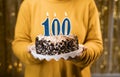 Woman holding birthday cake with number 100 candle, close up. One hundredth birthday or anniversary celebration