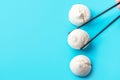 Woman holding black chop sticks in hand picking up home baked meringue cookies on blue background