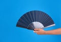 Woman holding black hand fan on light blue  background, closeup Royalty Free Stock Photo