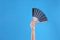 Woman holding black hand fan on light blue  background, closeup Royalty Free Stock Photo