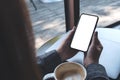 A woman holding black mobile phone with blank white desktop screen with coffee cup and laptop on table in cafe Royalty Free Stock Photo