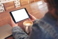 A woman holding black tablet pc with blank white screen horizontally with coffee cup and laptop on wooden table Royalty Free Stock Photo