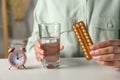 Woman holding blister of oral contraceptive pills and glass with water at white table, closeup Royalty Free Stock Photo