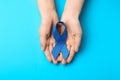 Woman holding blue awareness ribbon on color background. Symbol of social and medical issues