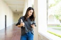 Woman Holding Books While Checking Social Site On Smartphone