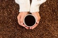 Woman holding with both hands a cup of black coffee on a heap of coffee grains