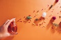 Woman holding bottle of perfume with ingredients. Fragrance of flowers, spices, herbs and fir tree on orange background