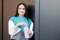 Woman holding bottle with water after morning workout. Young athletic woman standing near dark wall background after jogging