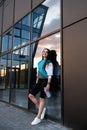 Woman holding bottle with water after morning workout. Young athletic woman standing near dark wall background after jogging