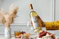 Woman holding bottle of white wine at table with snacks, closeup Royalty Free Stock Photo