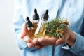 Woman holding bottles of essential oils and fir branches on white background