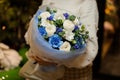 Woman holding a bouquet with blue and white flowers wrapped in matte transparent paper decorated with green leaves Royalty Free Stock Photo