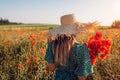 Woman holding bouquet of poppies flowers walking in summer field. Young girl in straw hat enjoys blooming landscape