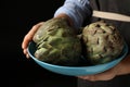 Woman holding bowl with fresh raw artichokes on black background, closeup Royalty Free Stock Photo