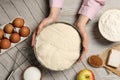 Woman holding bowl with fresh yeast dough and ingredients for cake on wooden table, closeup Royalty Free Stock Photo