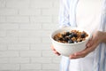 Woman holding bowl of oatmeal porridge with berries near white brick wall, closeup. Space for text Royalty Free Stock Photo