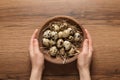 Woman holding bowl of quail eggs at wooden table, top view Royalty Free Stock Photo