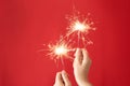 Woman holding bright burning sparklers on red background, closeup Royalty Free Stock Photo